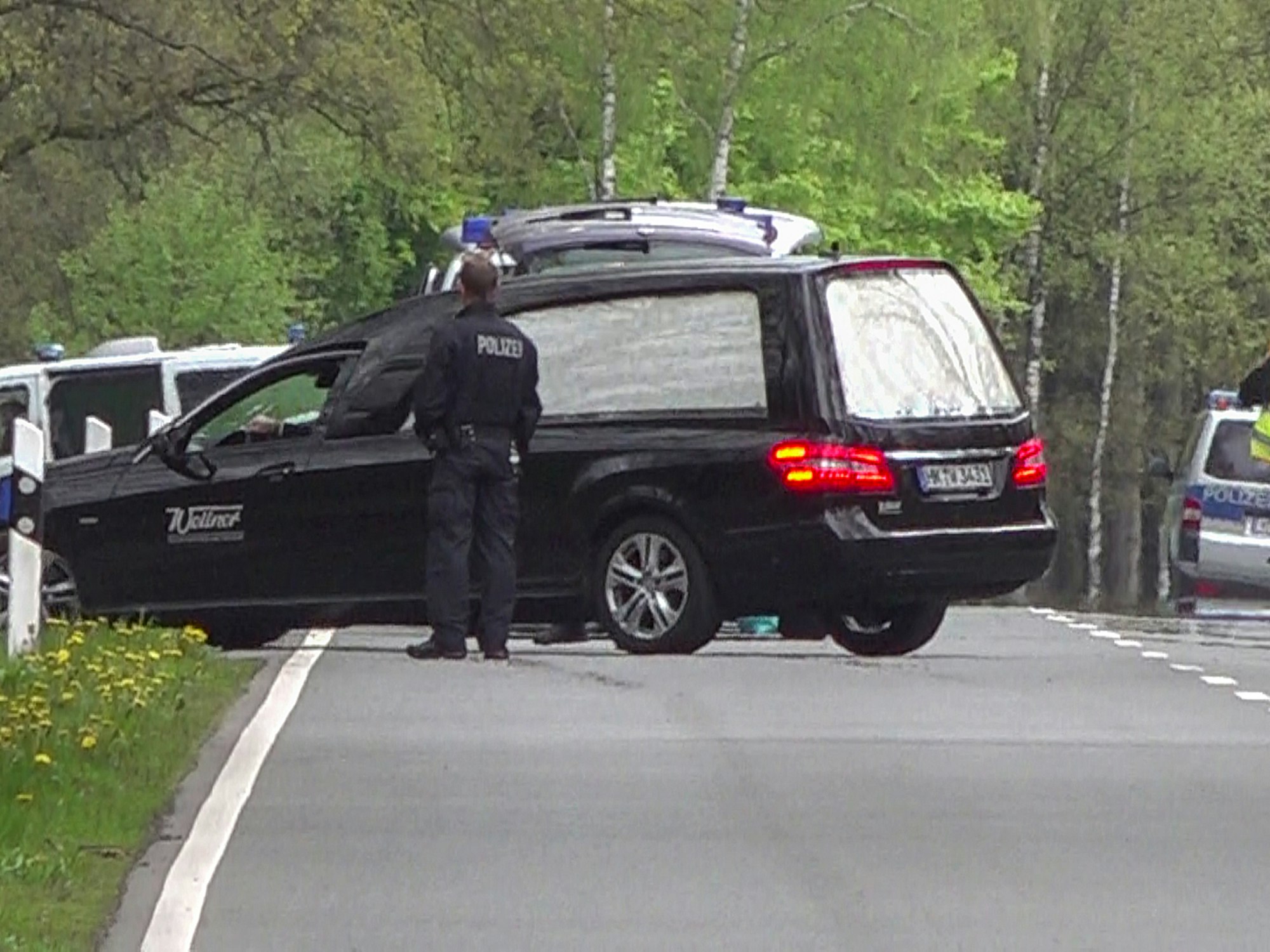 Hier zu sehen, ein Leichenwagen am Straßenrand, umringt von mehreren Polizeiautos.