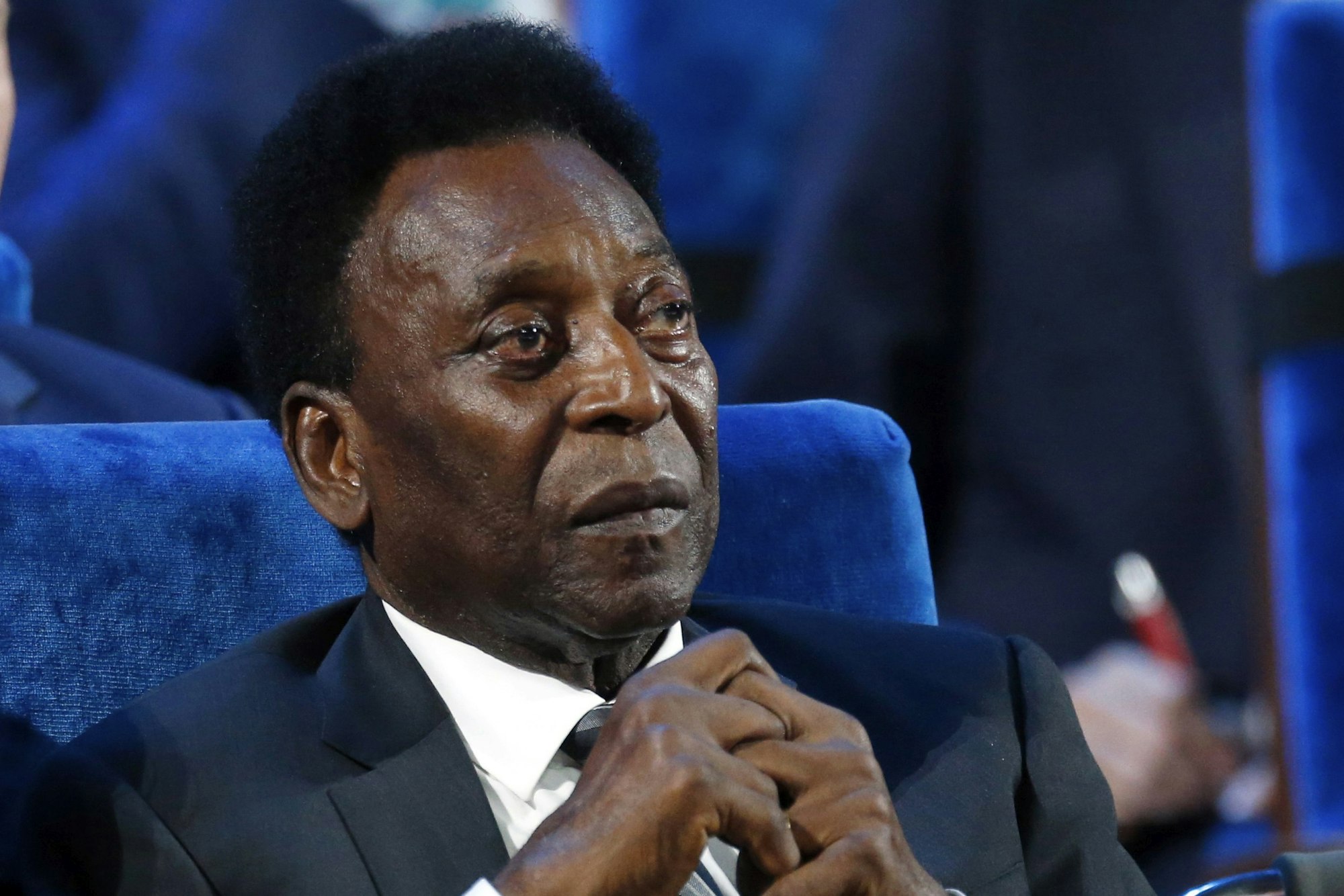 Pele sitzt mit verschränkten Fingern in einem blauen Sessel