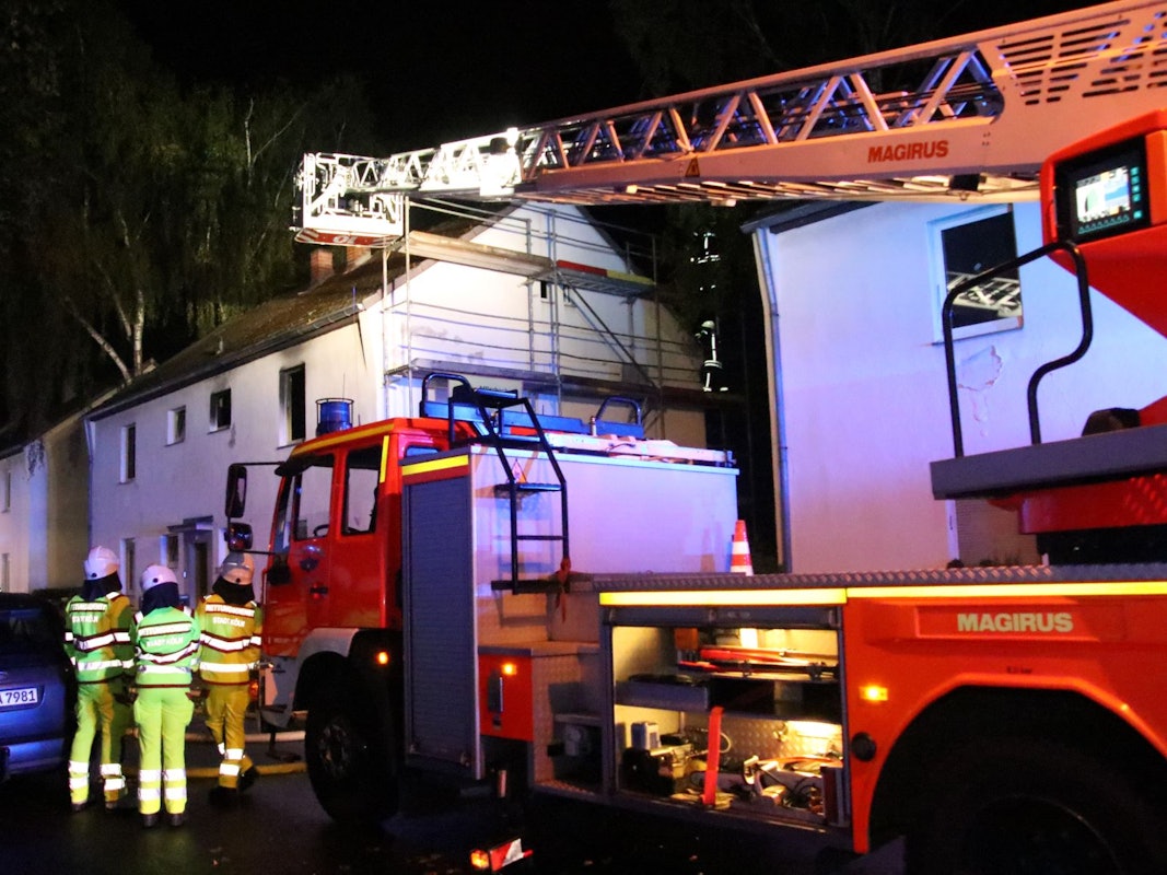 Einsatzkräfte der Feuerwehr sind mit einem Drehleiter-Wagen vor dem Brandhaus.