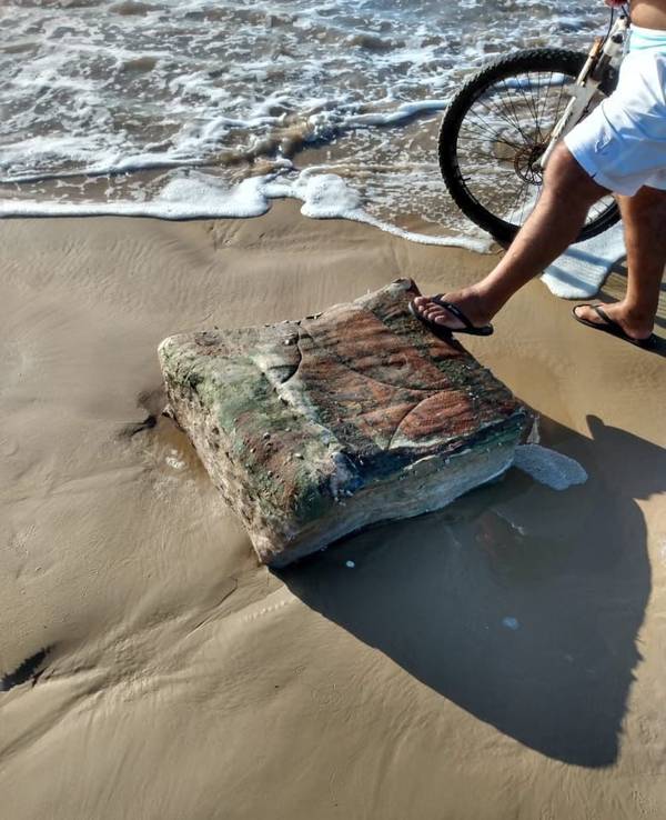 Ein Passant stellt seinen Fuß am Strand von Brasilien auf eine mysteriöse Kiste