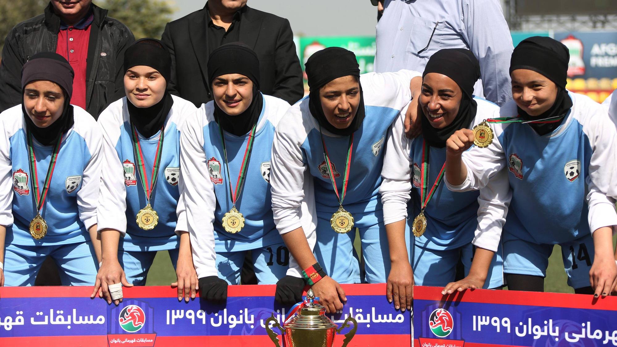 Sechs Spielerinnen von Herat sind zu sehen. Sie tragen Trikots, Kopftücher und Medaillen. Vor ihnen steht der Pokal.
