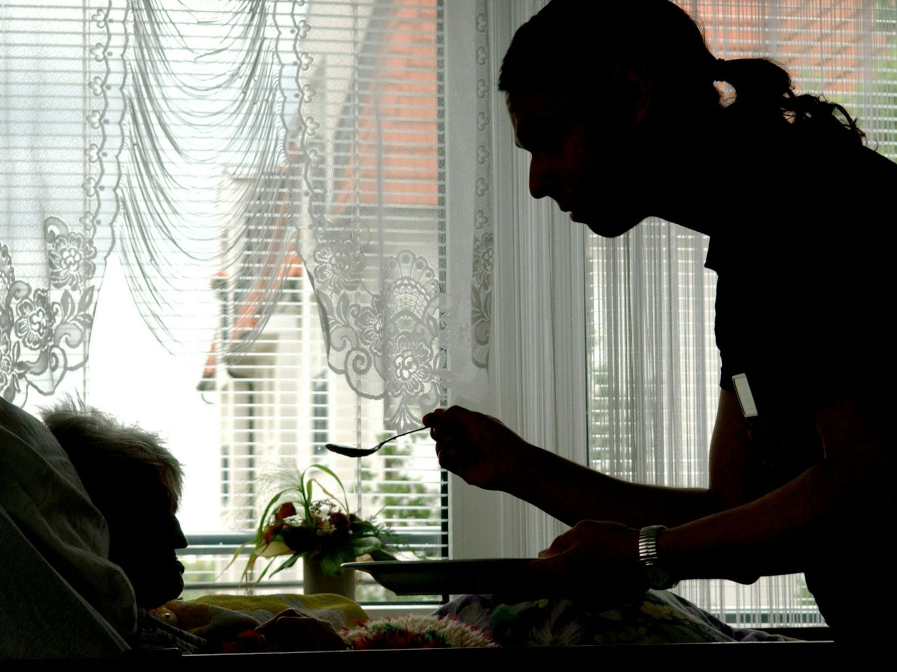 Ein Altenpfleger reicht einer Seniorin Essen.
