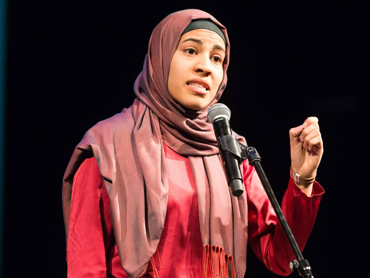 Nemi El-Hassan steht in Braunschweig in einem roten Kleid und mit rotem Kopftuch am Mikrofon auf einer Bühne bei einem Poetry Slam.
