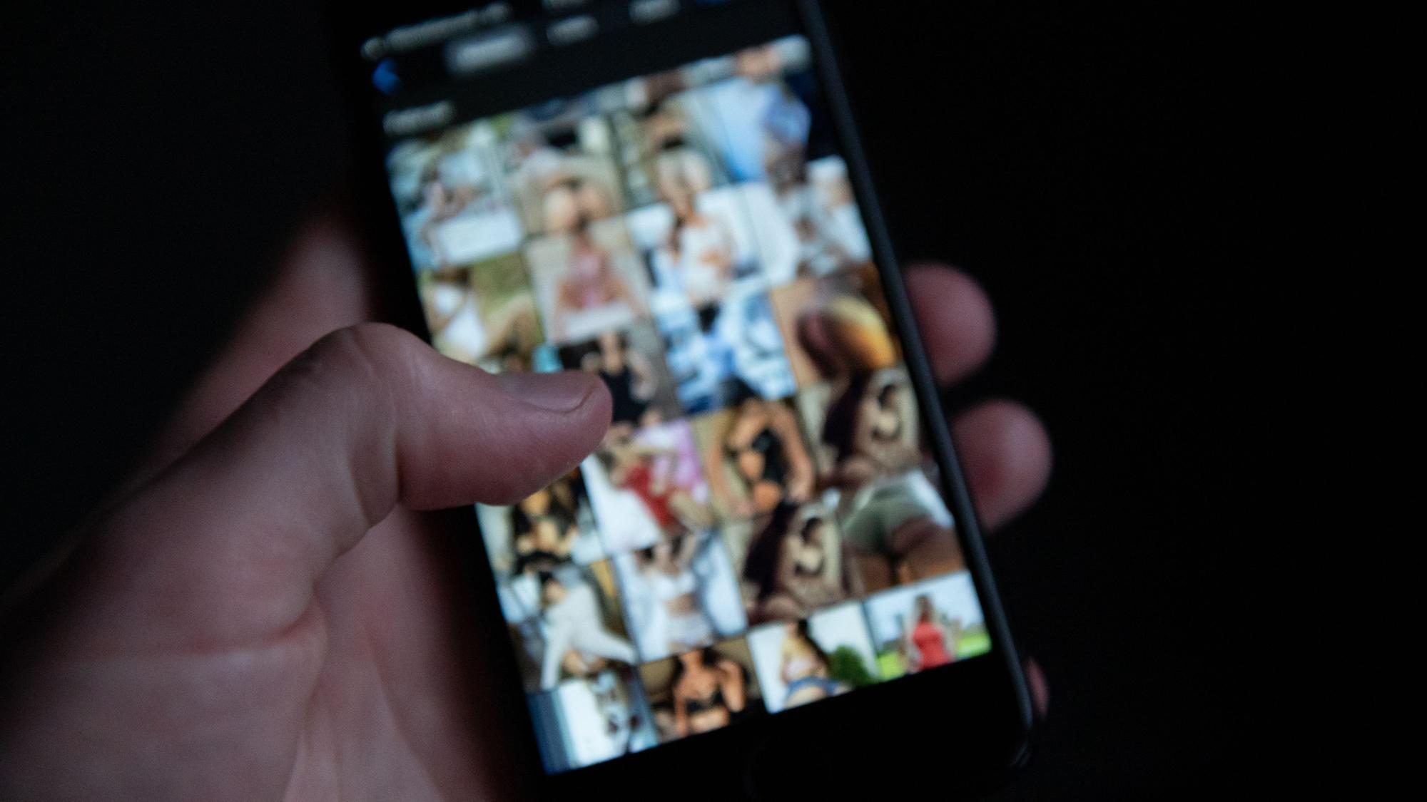 Eine Hand scrollt auf einem Handy herum, auf dem mehrere pornografische Bilder verschwommen zu sehen sind.