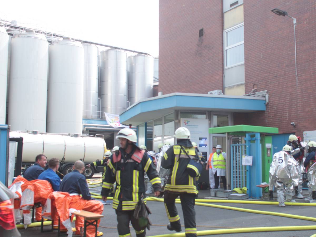 Feuerwehrmänner und Männer in Spezialanzügen befinden sich vor einem Werk.