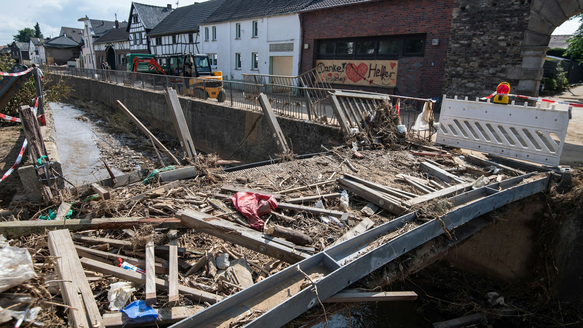 Zerstört ist diese Brücke über den Orbach. Nach der Flutkatastrophe laufen in den betroffenen Regionen in NRW neben den Aufbauarbeiten (wie hier am 27. Juli 2021 in Swisttal) nun auch die Aufbauhilfen.