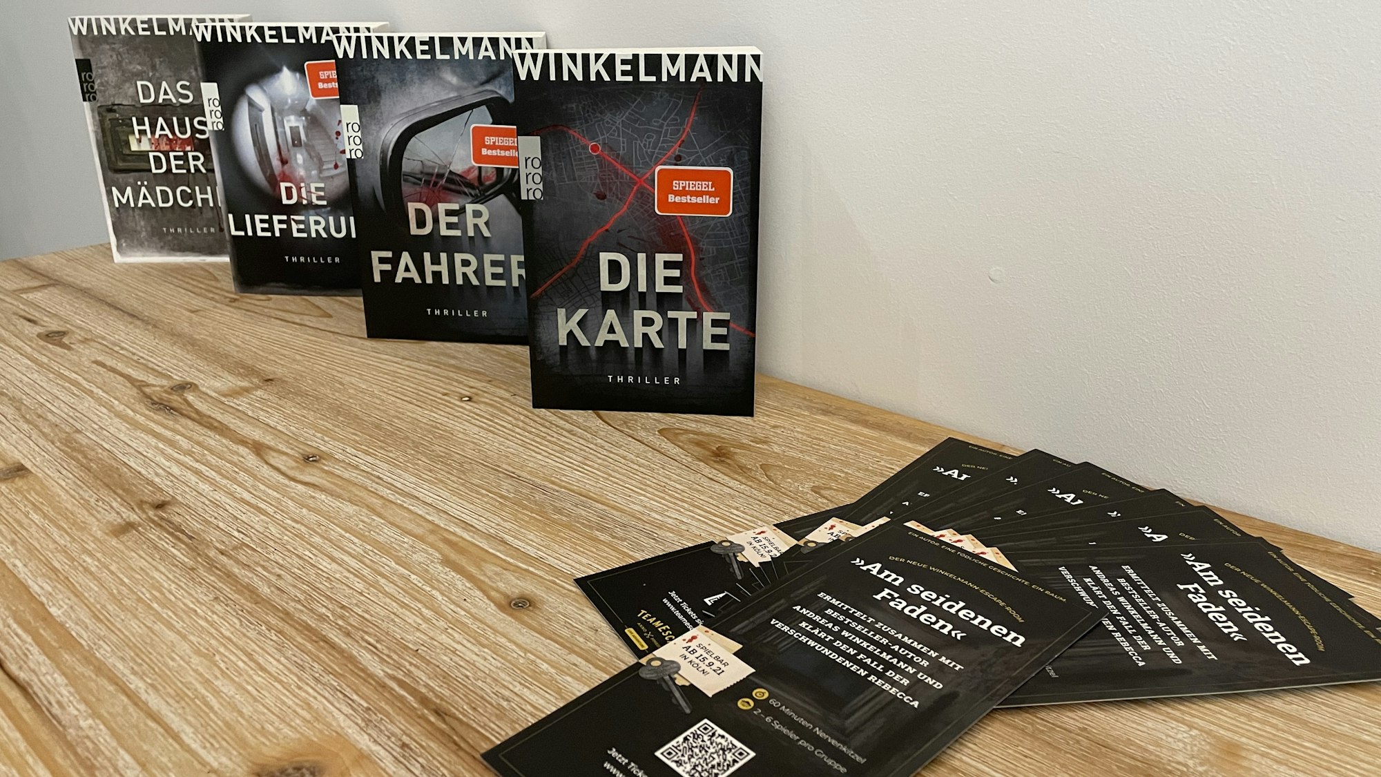 Die vier Bücher der Thriller-Reihe von Andreas Winkelmann stehen auf einem Tisch, davor liegen Flyer zum neuen Escape Room.
