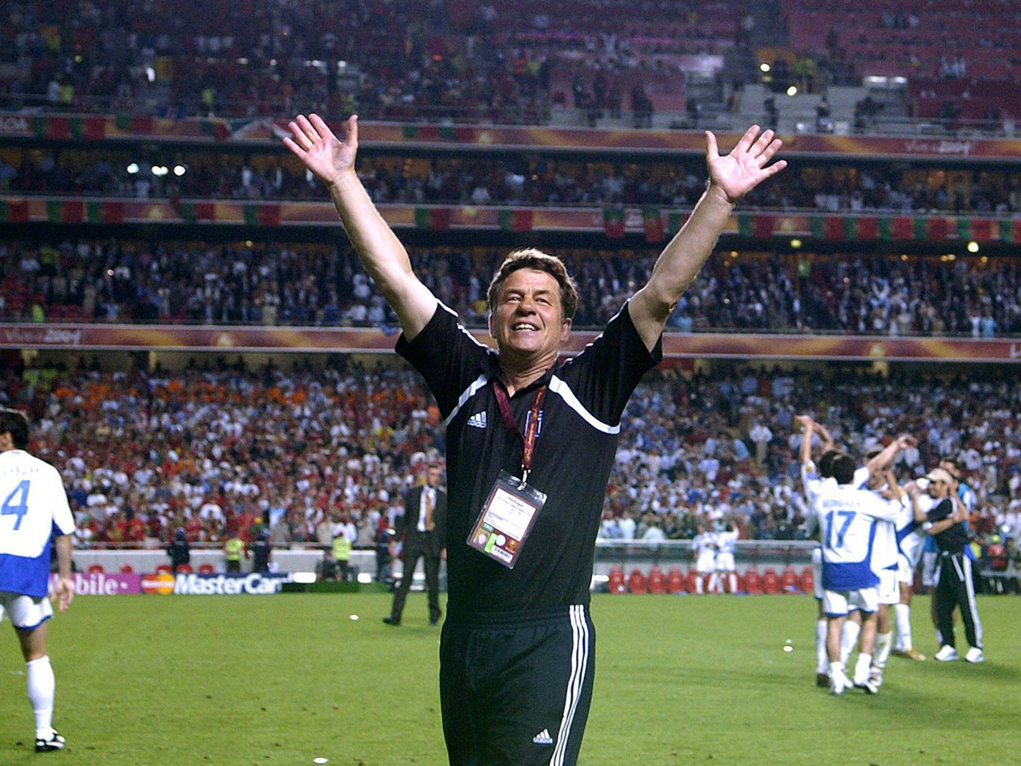 Rehhagel steht auf dem Platz und reißt vor Freude seine Arme in die Luft.