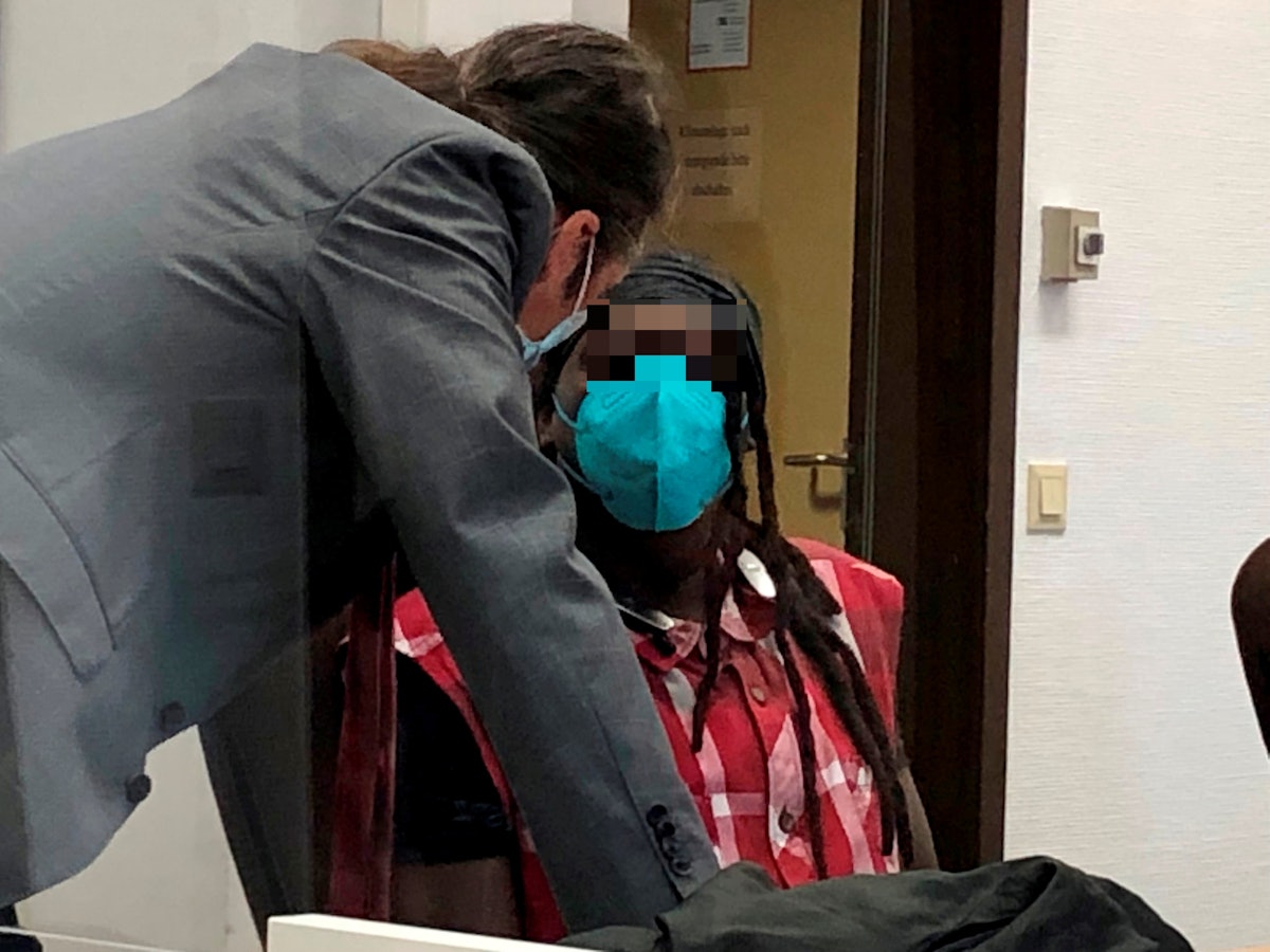 Ein Mann sitzt auf der Anklagebank, sein Verteidiger beugt sich zu ihm runter.