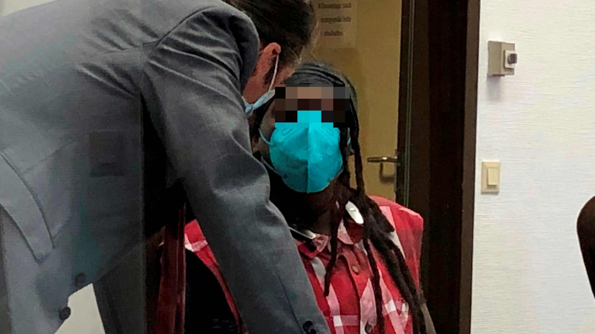 Ein Mann sitzt auf der Anklagebank, sein Verteidiger beugt sich zu ihm runter.