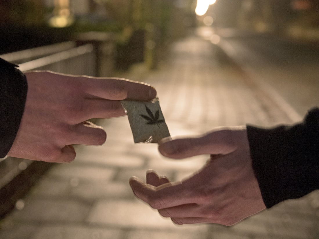 Ein Mann übergibt ein Tütchen mit Marihuana an einen anderen.