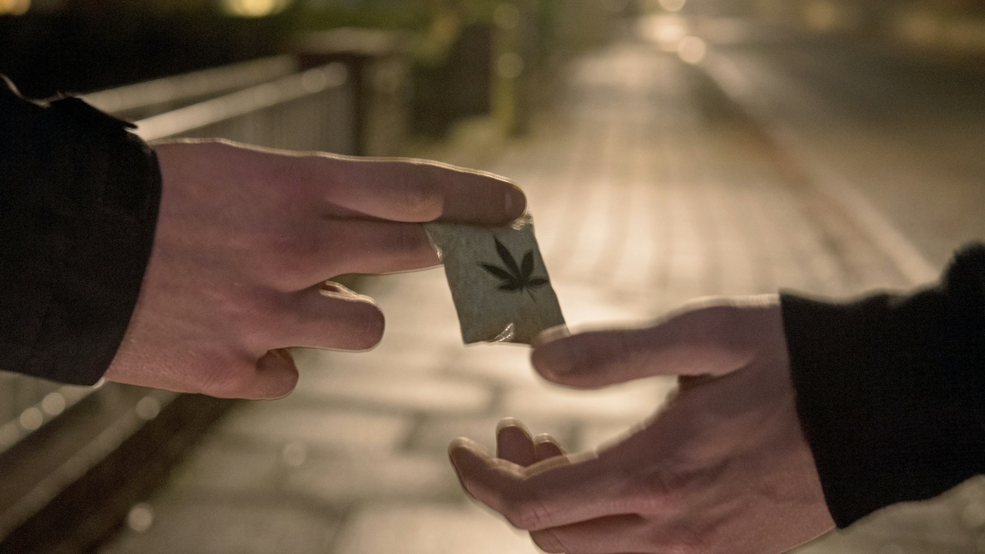 Ein Mann übergibt ein Tütchen mit Marihuana an einen anderen.