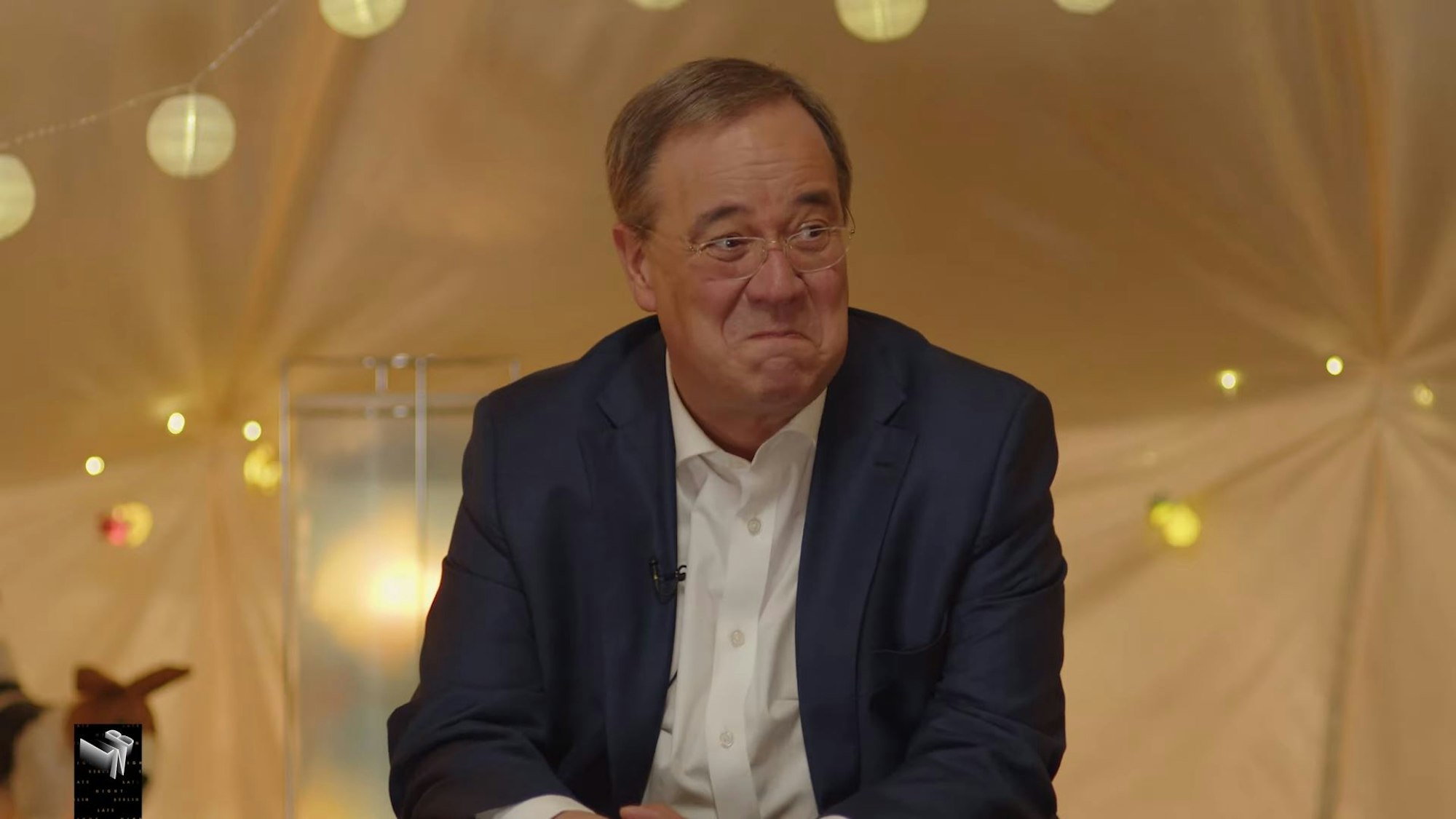 Armin Laschet sitzt im Zelt mit den beiden Kinderreportern Pauline und Romeo und verzieht erstaunt sein Gesicht.