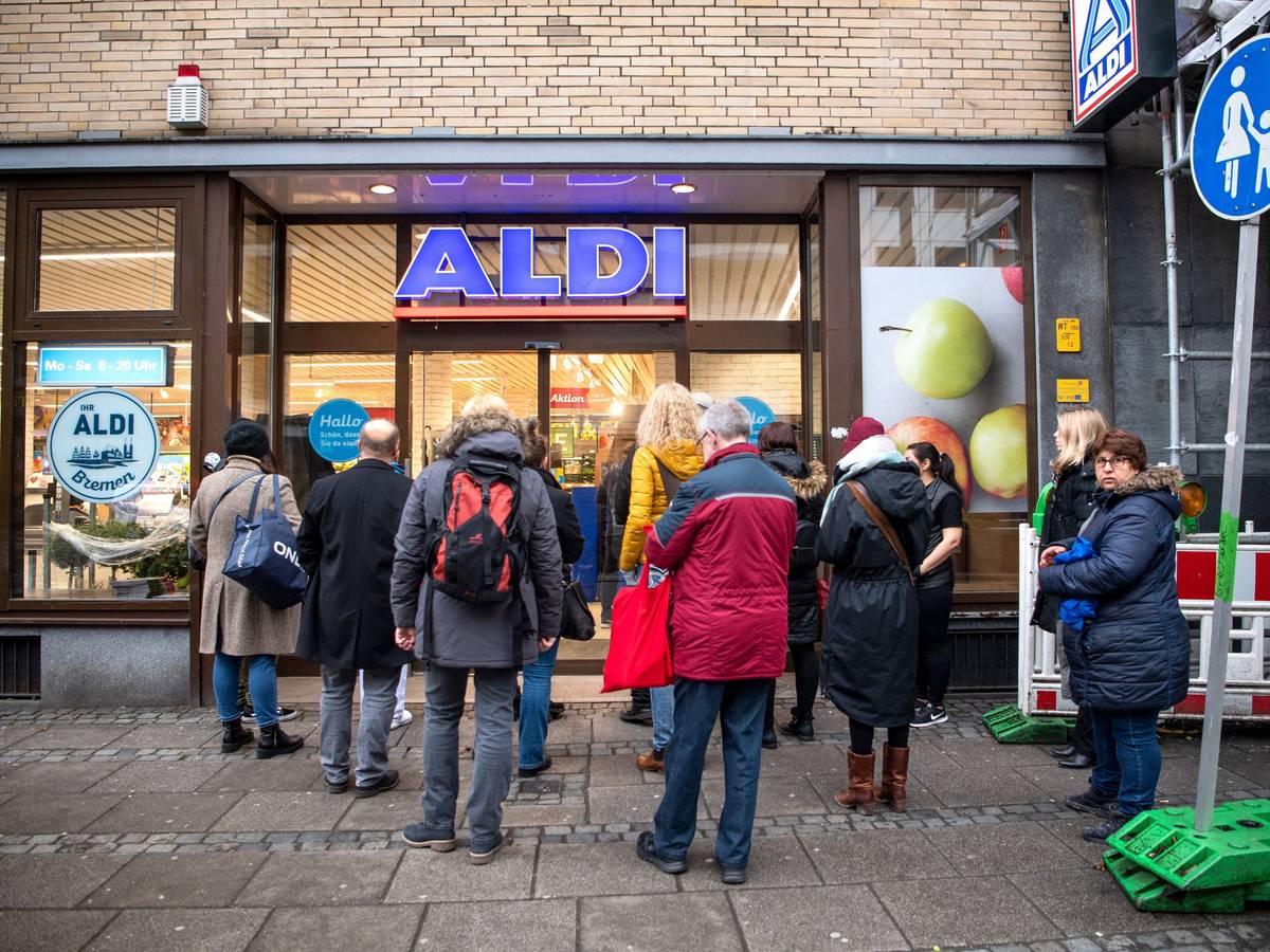 Kunden stehen am frühen Morgen kurz vor Öffnung vor einem Aldi-Markt.