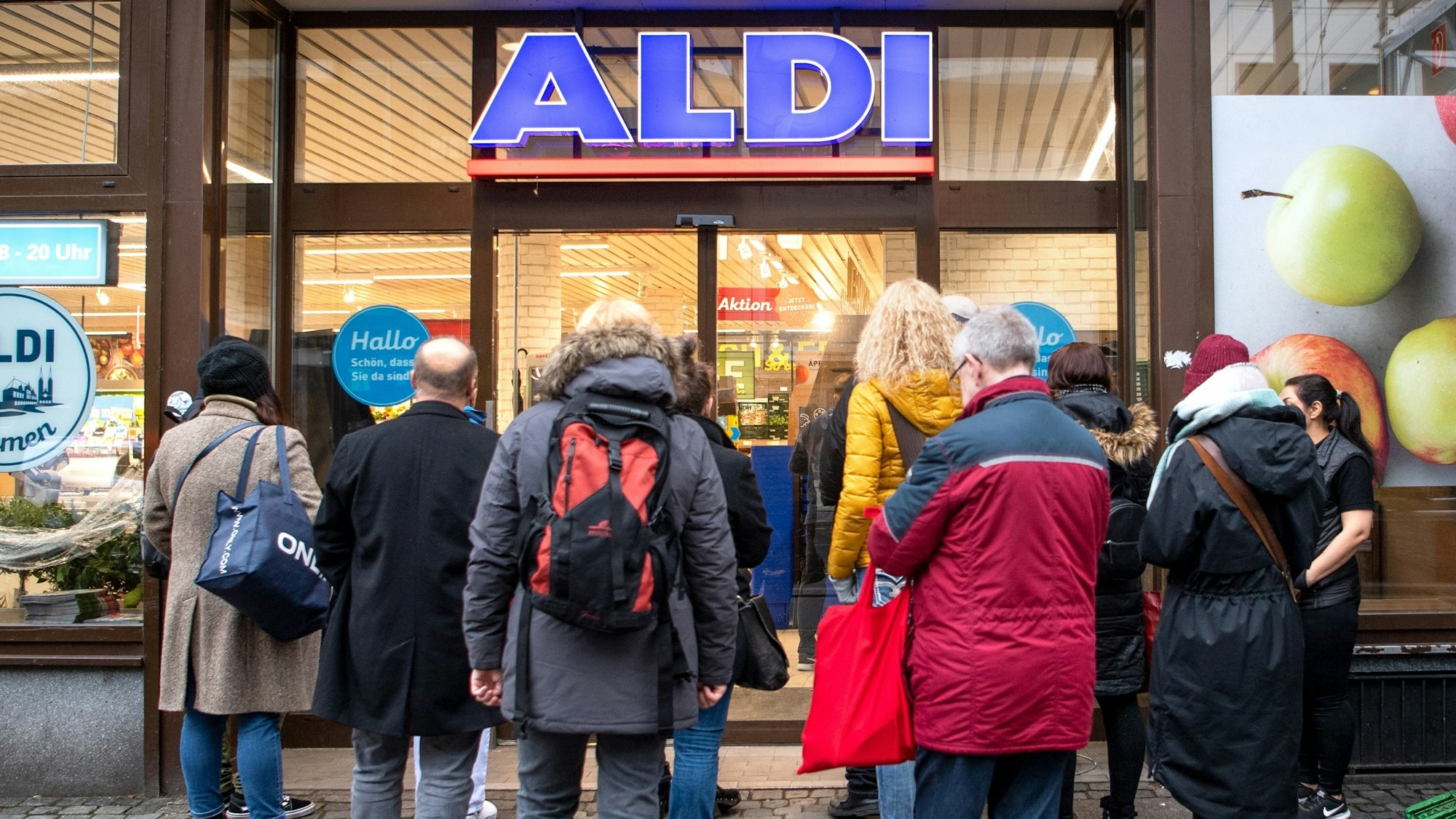 Kunden stehen am frühen Morgen kurz vor Öffnung vor einem Aldi-Markt.