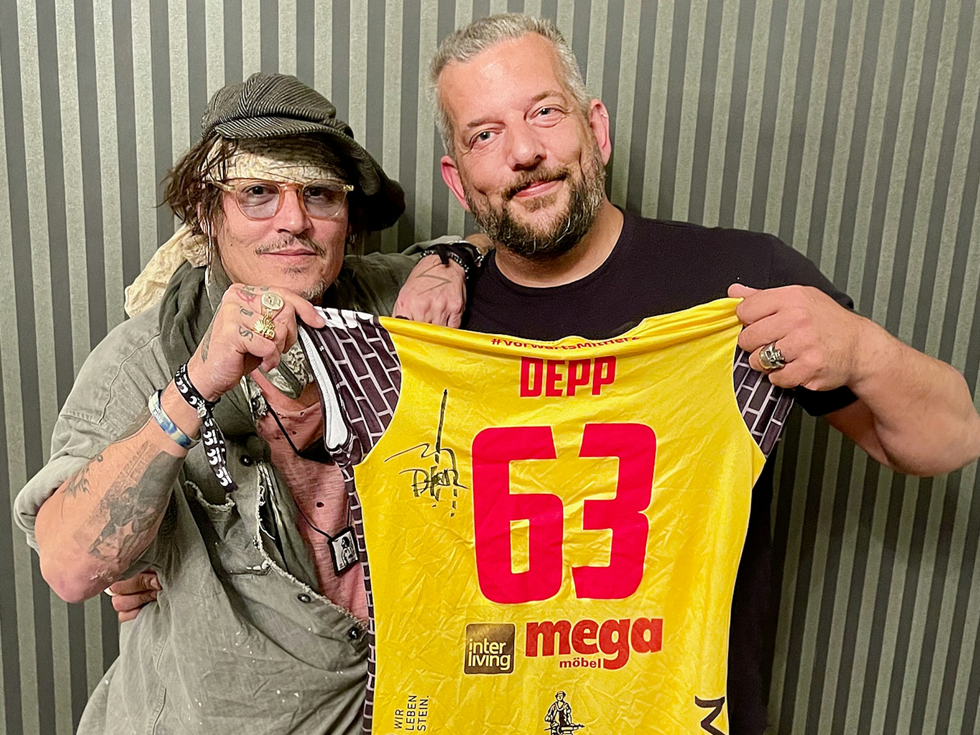 Johnny Depp und der in Suhl lebende Musiker Alexander Becker halten zusammen ein Trikot des Volleyball-Bundesligistes VfB Suhl.
