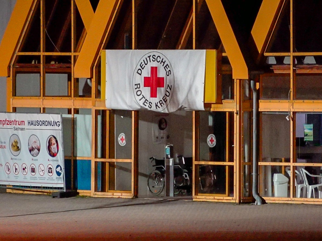 Eine Rot-Kreuz-Fahne hängt über dem Eingang zum Impfzentrum in Eich. Im sächsischen Vogtlandkreis hat es einen Brandanschlag auf ein Impfzentrum gegeben.