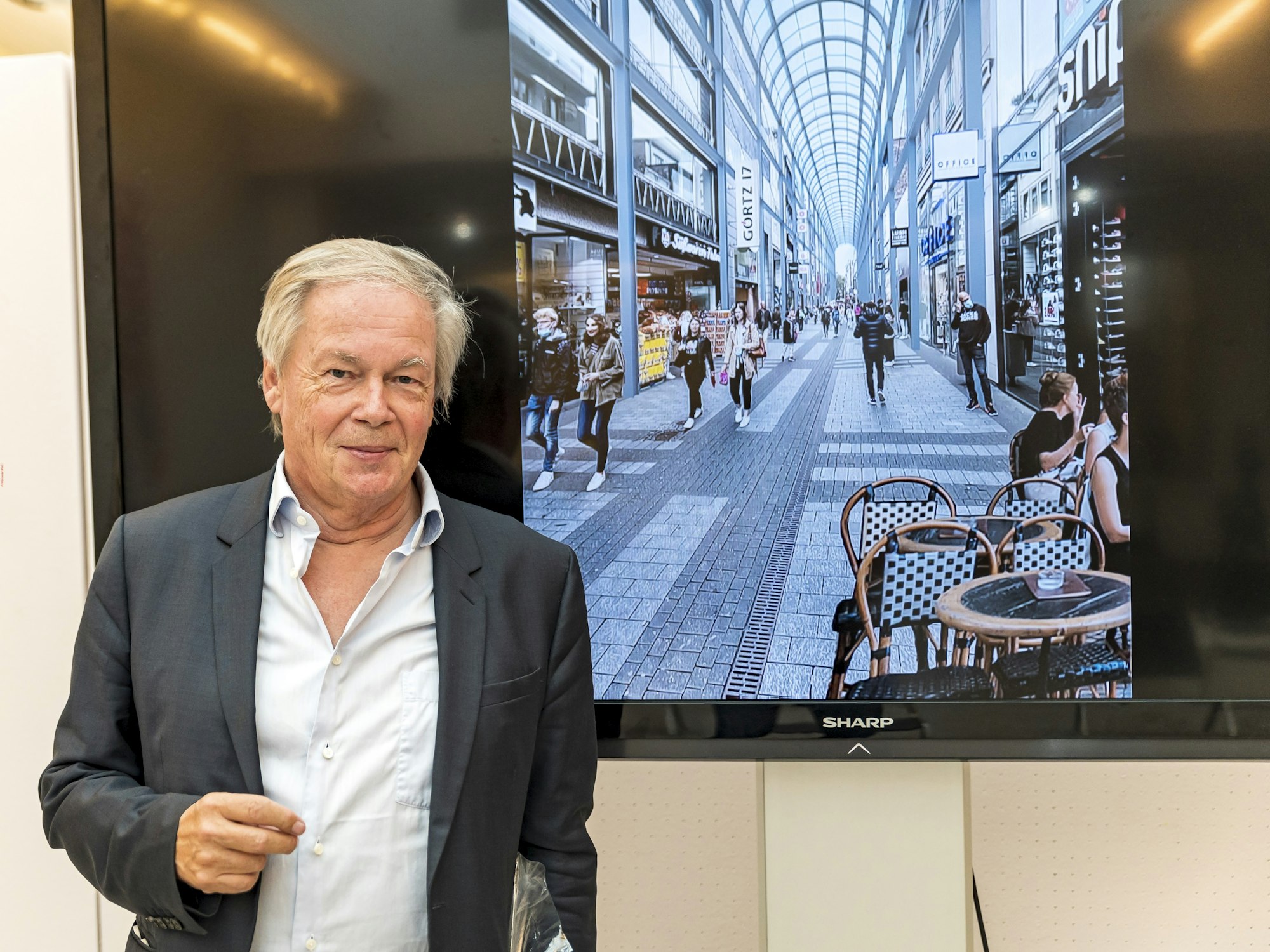 Architekt Prof. Stephan Braunfels vor einem Fernseher mit der Illustration der Hohe Straße mit einem Glasdach.