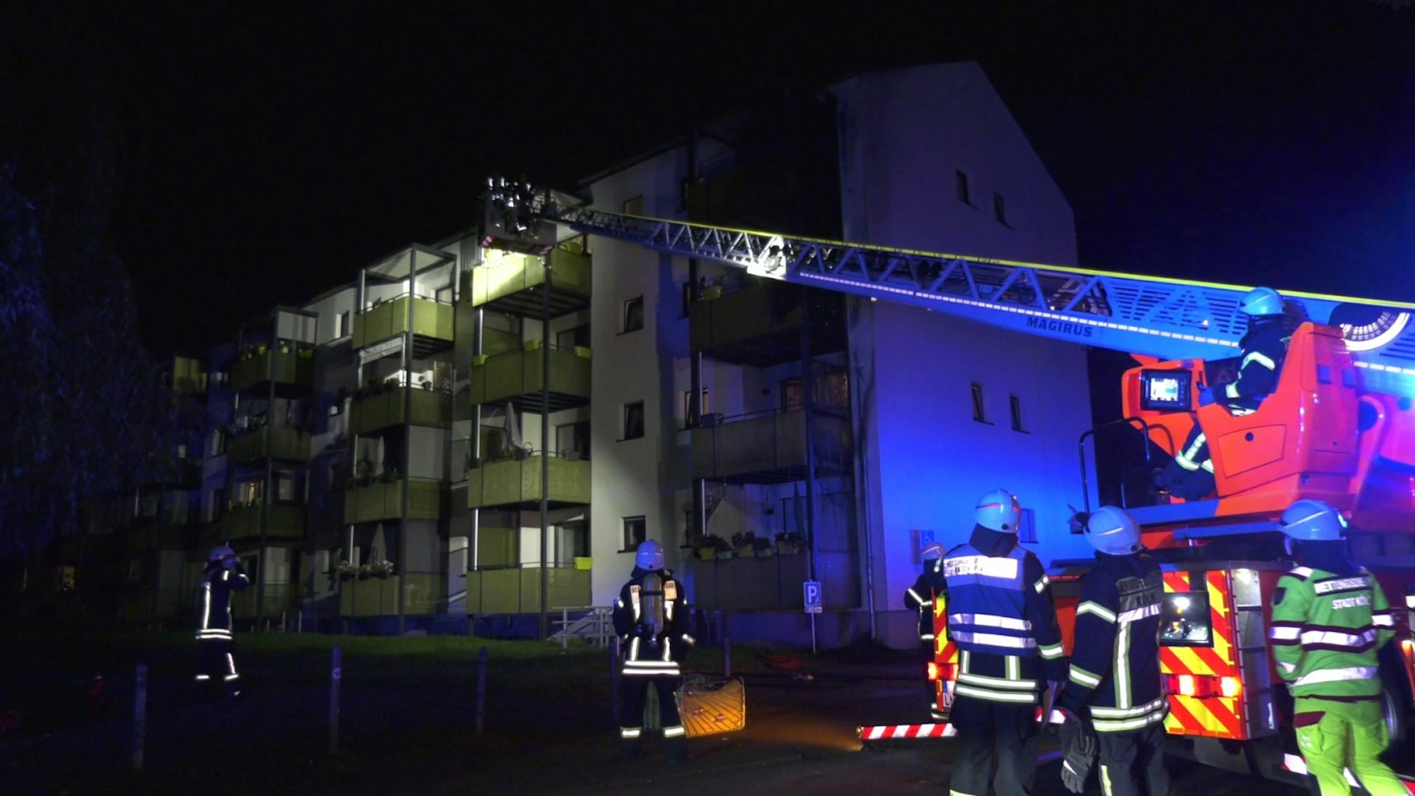 Feuerwehr mit einigen Einsatzkräften vor einem Mehrfamilienhaus in Köln. Die Drehleiter ist ausgefahren.
