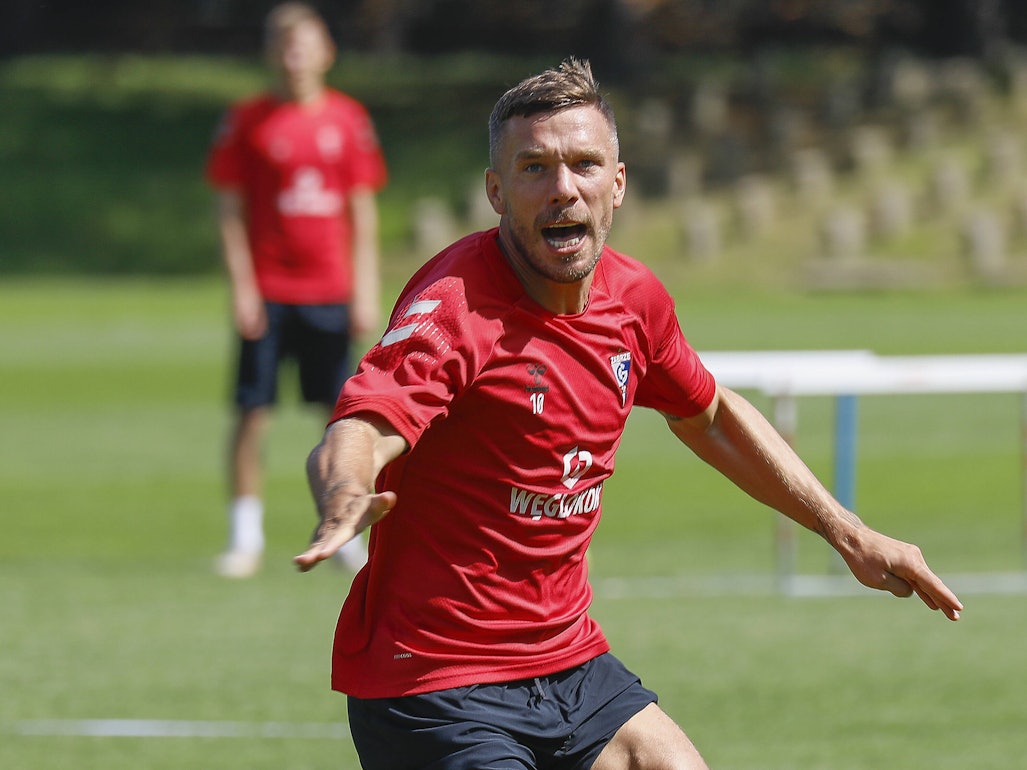 Podolski reißt auf dem Trainingsplatz den Mund auf und breitet die Arme auf.