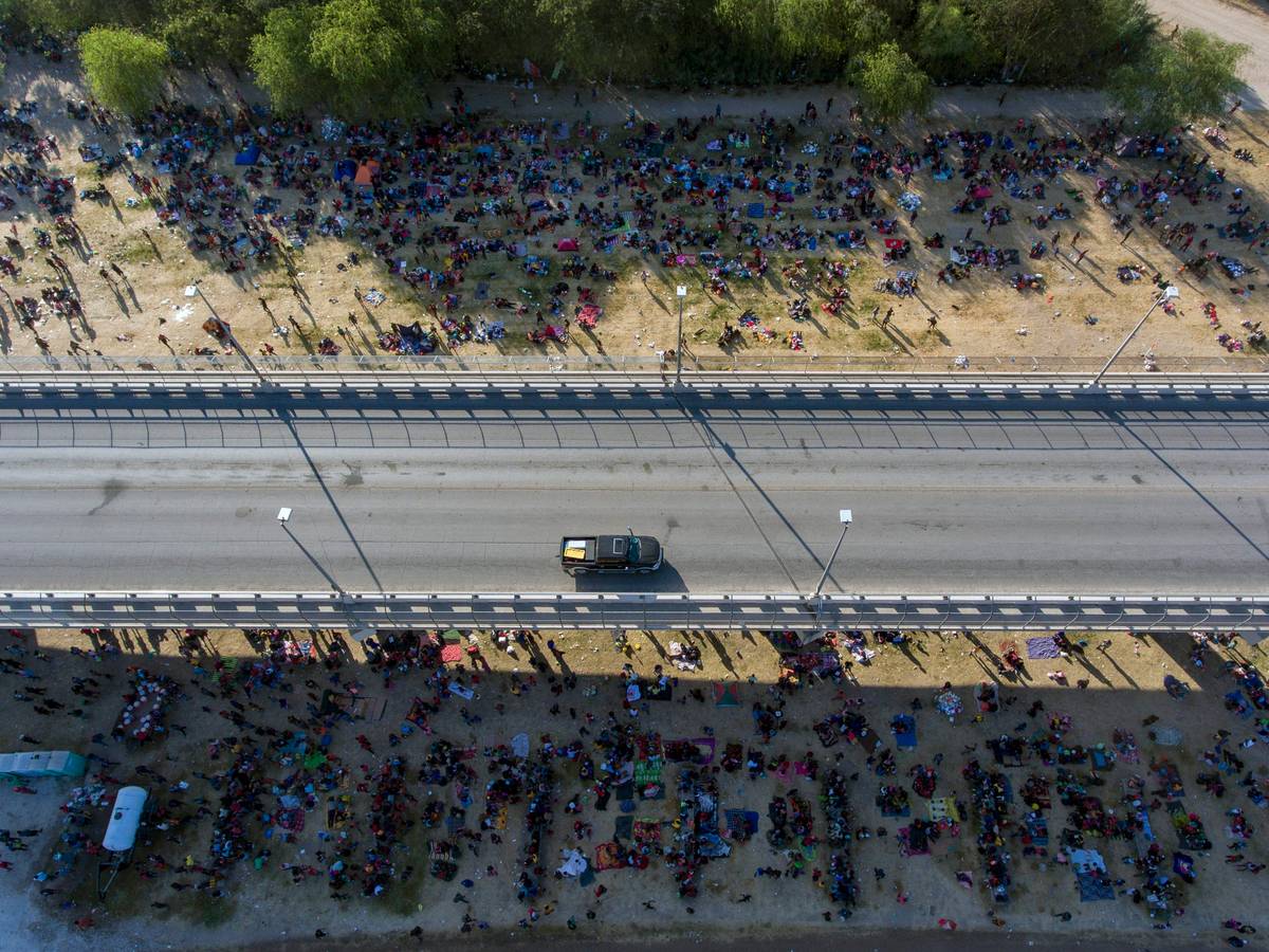 Migranten kampieren unter einer Brücke in Del Rio. Eine Straße ist von oben zu sehen, an der Seite sind unzählige Menschen zu sehen, die dort im Schatten der Brücke verbleiben.