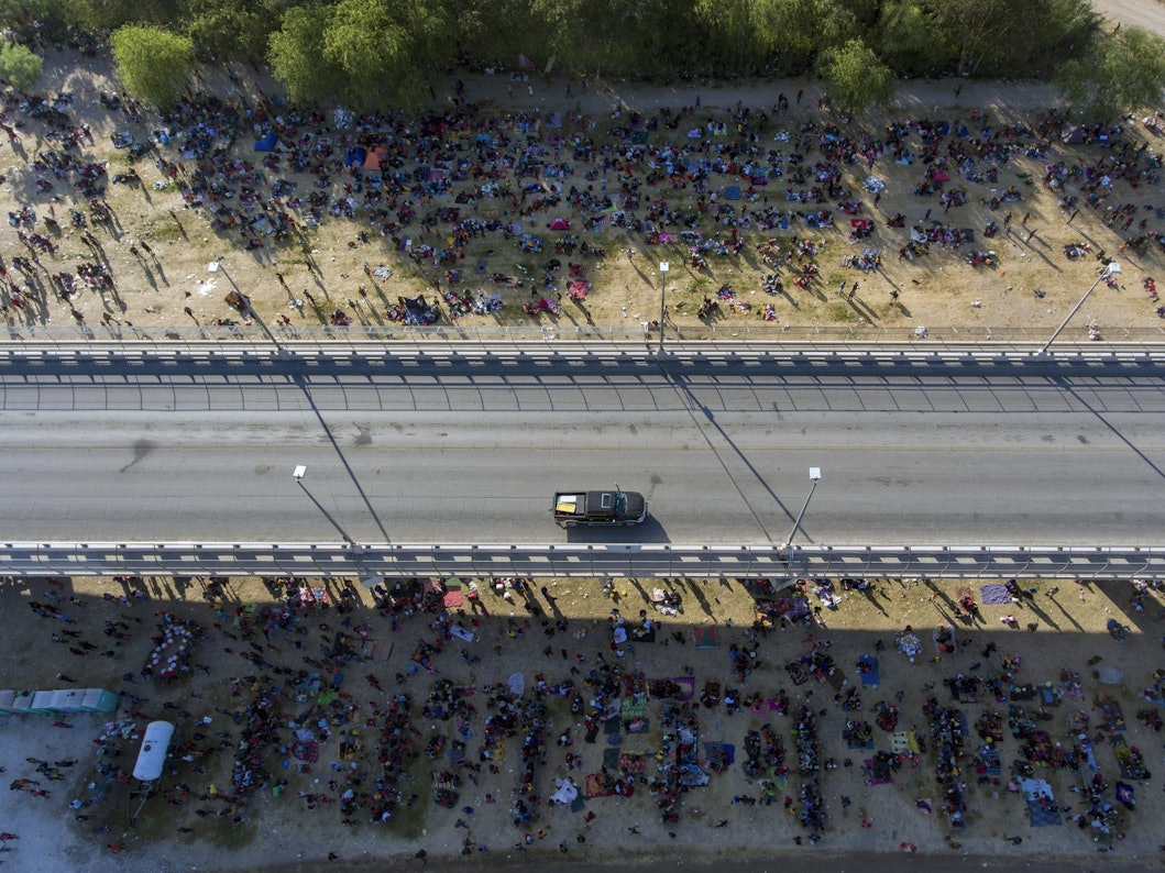 Migranten kampieren unter einer Brücke in Del Rio. Eine Straße ist von oben zu sehen, an der Seite sind unzählige Menschen zu sehen, die dort im Schatten der Brücke verbleiben.