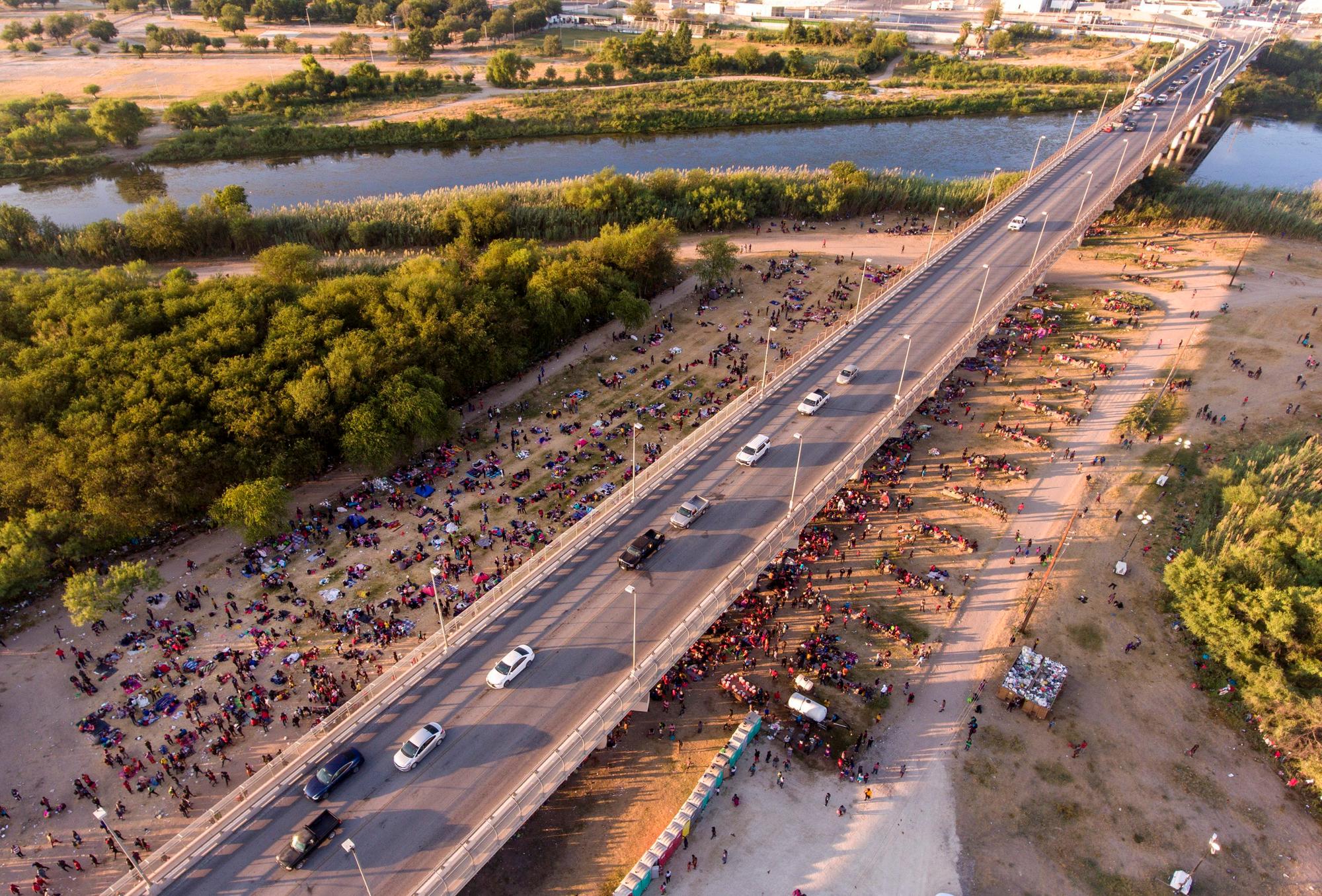 Migranten kampieren unter einer Brücke in Del Rio. Eine Straße ist von oben zu sehen, an der Seite sind unzählige Menschen zu sehen, die dort im Schatten der Brücke verbleiben.