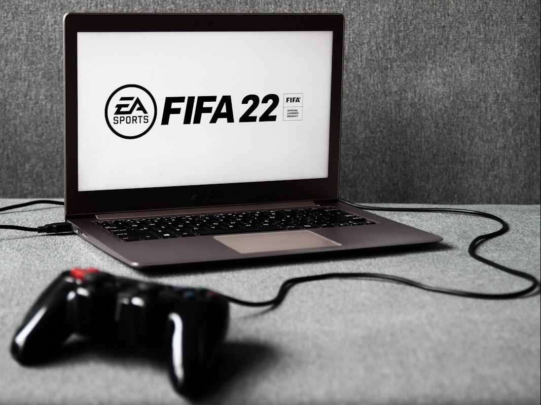 Ein Laptop, auf dem das EA-Logo und der Schriftzug FIFA 22 zu sehen ist. Davor liegt ein Controller.