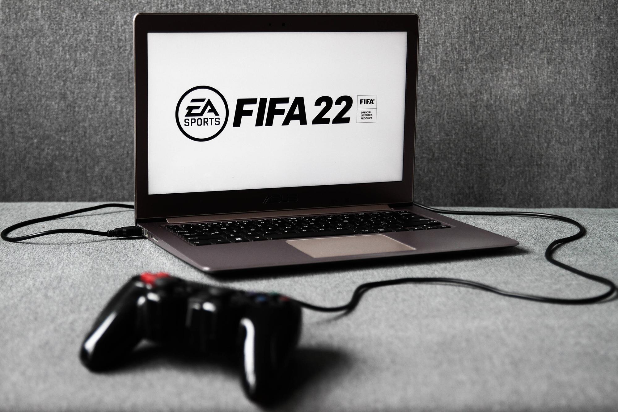 Ein Laptop, auf dem das EA-Logo und der Schriftzug FIFA 22 zu sehen ist. Davor liegt ein Controller.