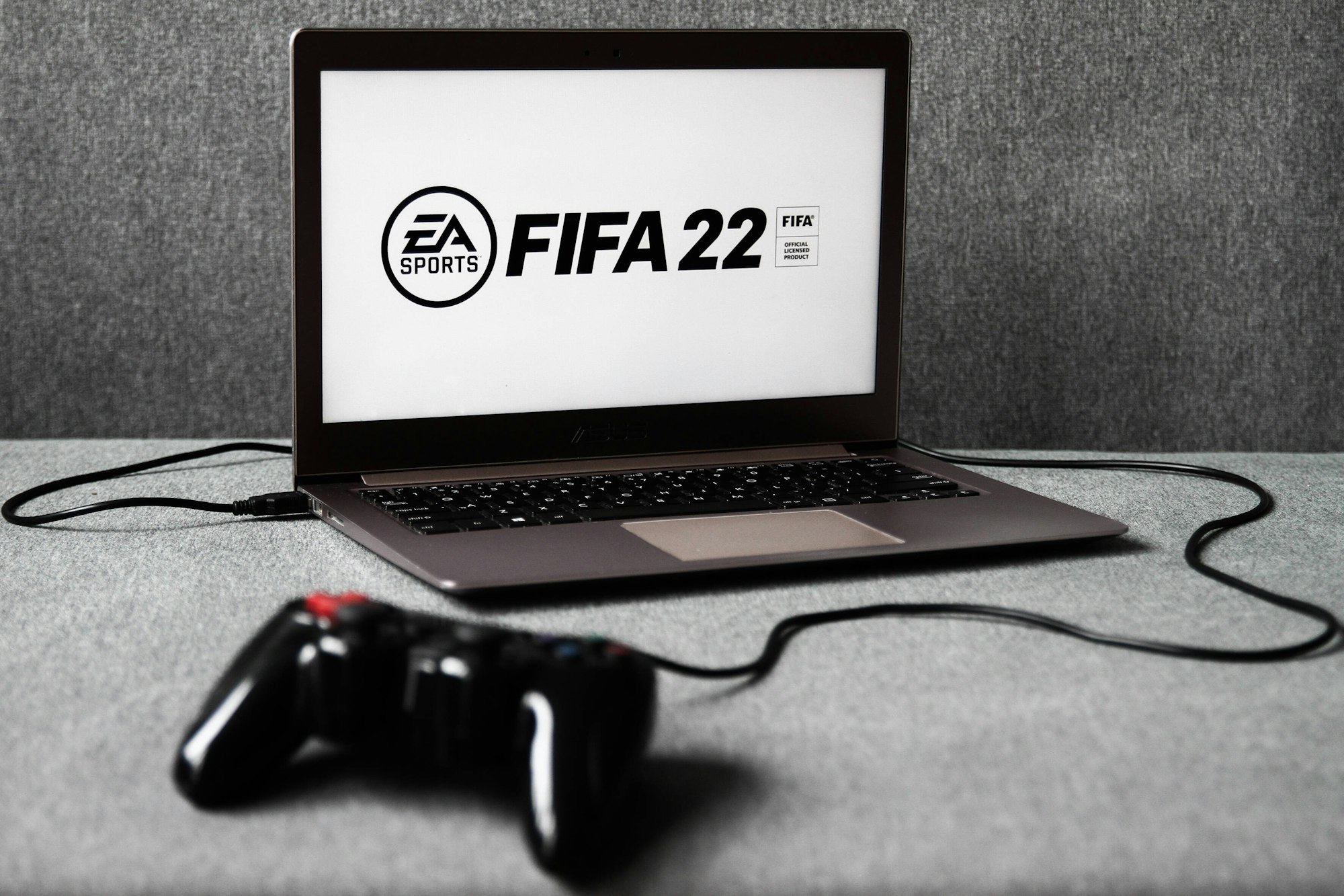 Ein Laptop, auf dem das EA-Logo und der Schriftzug FIFA 22 zu sehen ist. Davor liegt ein Controller.