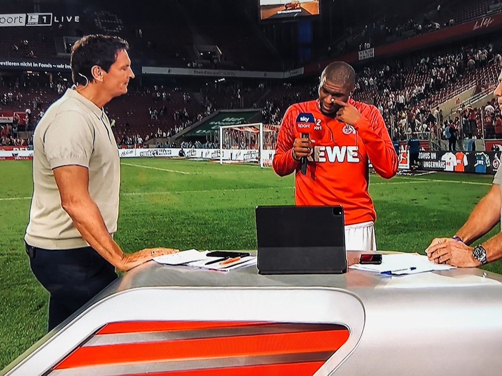 Anthony Modeste weint beim Sky-Interview mit Sebastian Hellmann (l.) und Lothar Matthäus (r.) am 18. September 2021 nach dem 1:1 des 1. FC Köln gegen RB Leipzig.