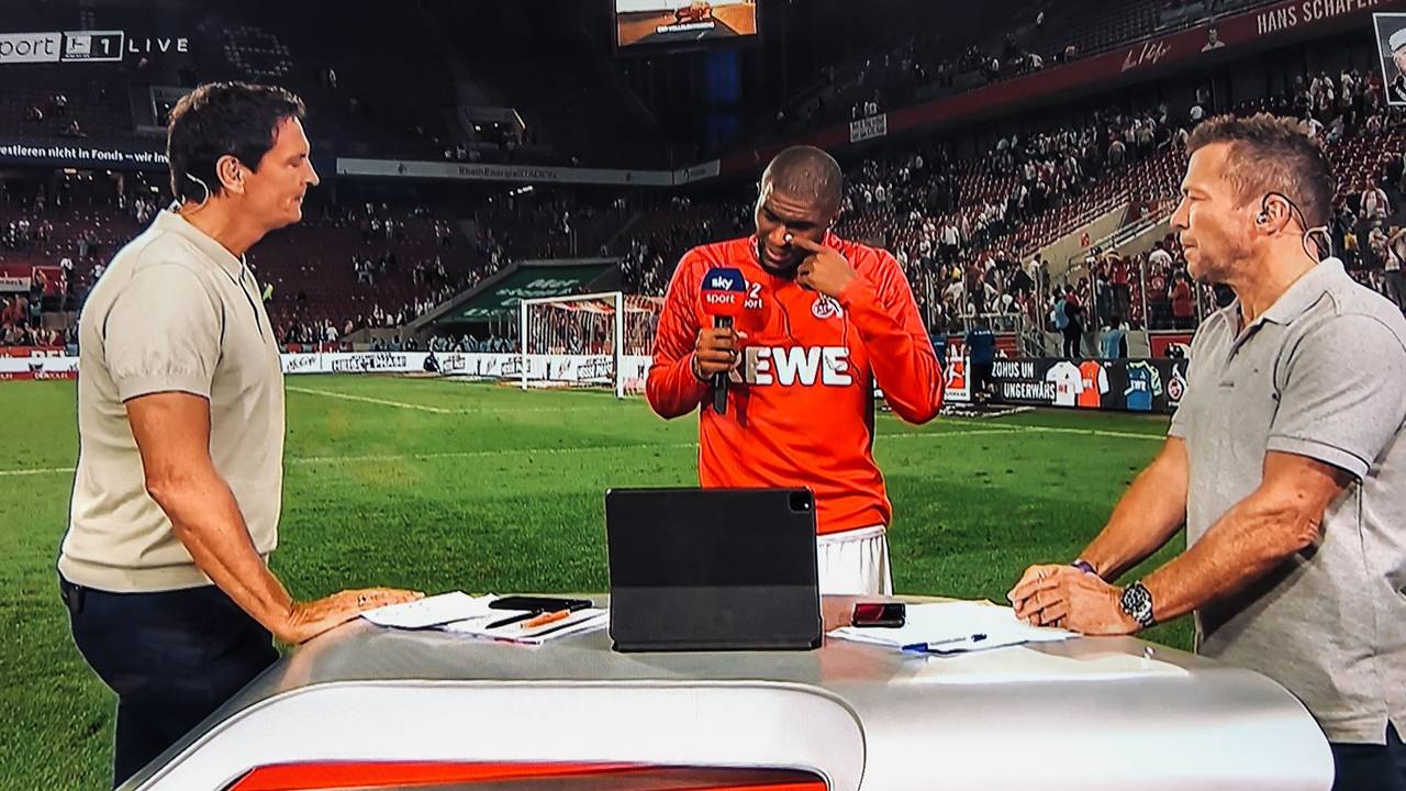Anthony Modeste weint beim Sky-Interview mit Sebastian Hellmann (l.) und Lothar Matthäus (r.) am 18. September 2021 nach dem 1:1 des 1. FC Köln gegen RB Leipzig.