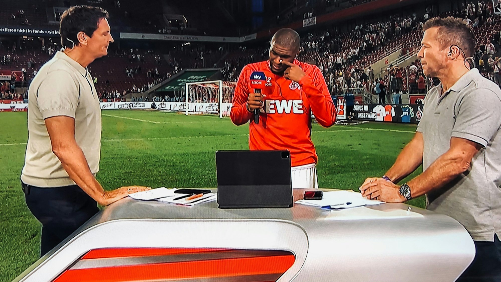 Anthony Modeste weint beim Sky-Interview mit Sebastian Hellmann (l.) und Lothar Matthäus (r.) am 18. September 2021 nach dem 1:1 des 1. FC Köln gegen RB Leipzig als er über seinen verstorbenen Vater Guy spricht.