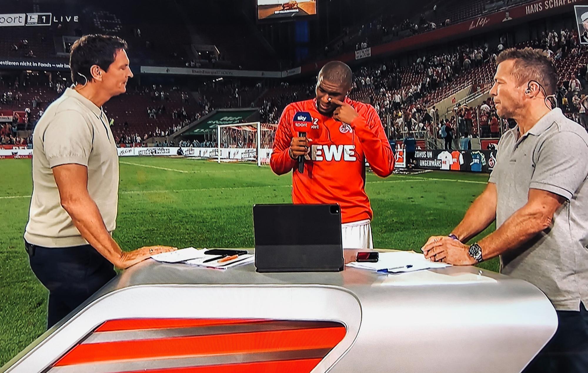 Anthony Modeste weint beim Sky-Interview mit Sebastian Hellmann (l.) und Lothar Matthäus (r.) am 18. September 2021 nach dem 1:1 des 1. FC Köln gegen RB Leipzig.