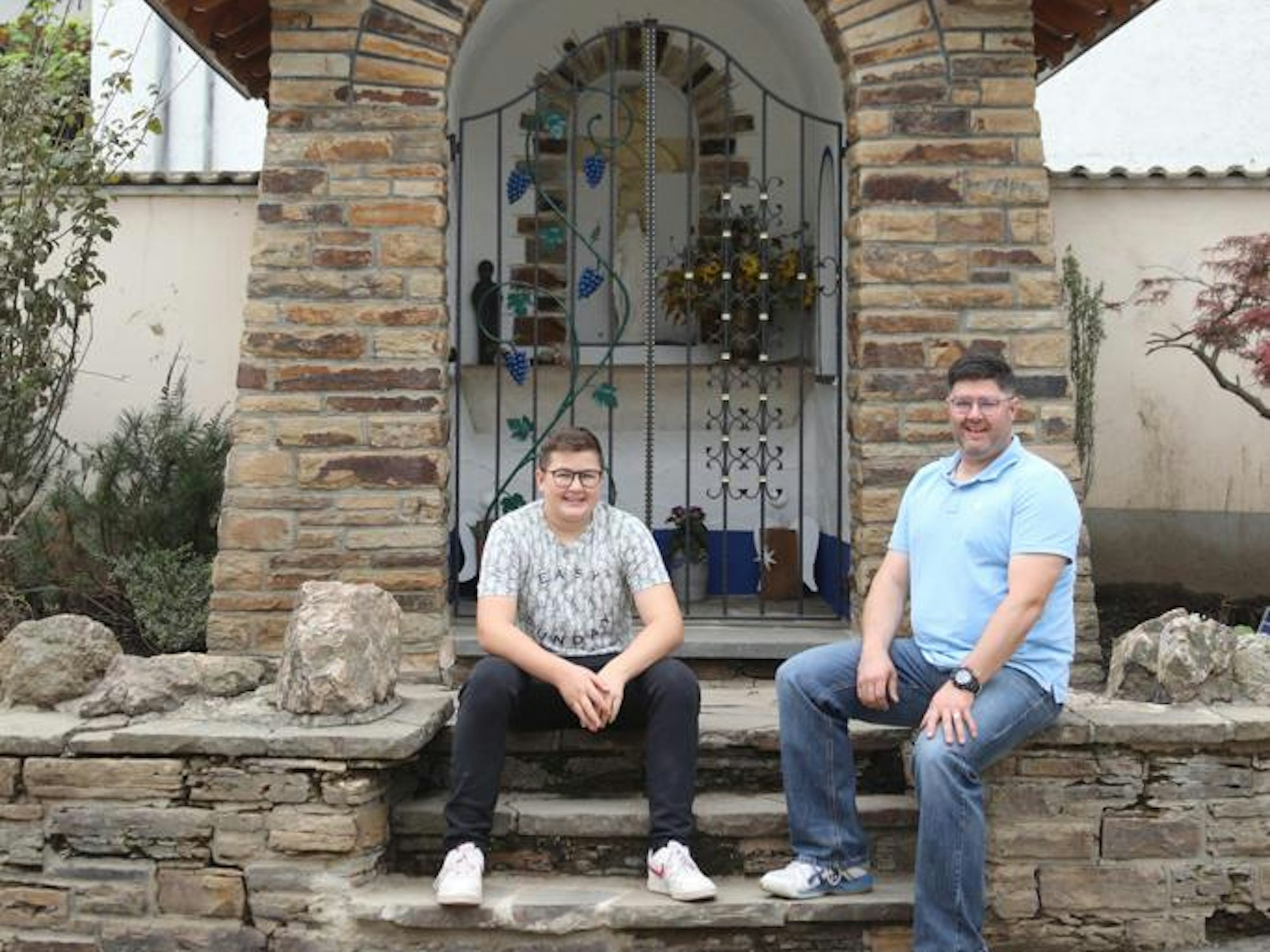 Christian und Arne Schrading sitzen vor der Kapelle an der Hauptstraße in Dernau.