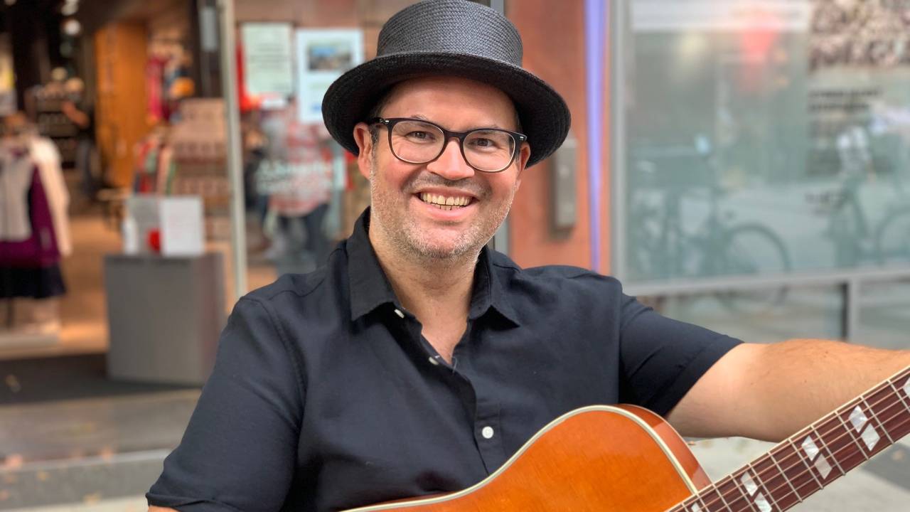 Björn Heuser hält eine Gitarre in der Hand.