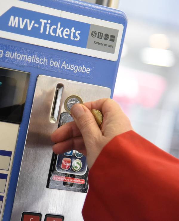 Eine Person wirft Münzen in einen Automaten des Münchner Verkehrs- und Tarifverbunds