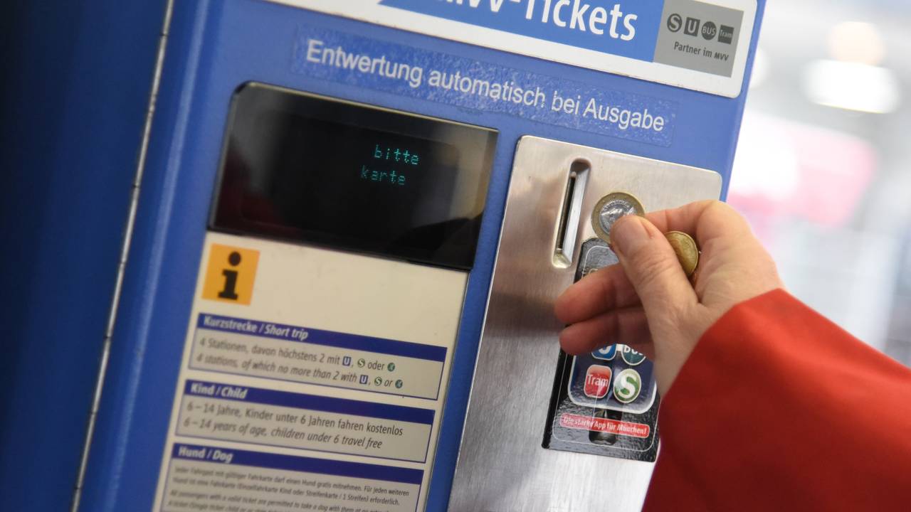 Eine Person wirft Münzen in einen Automaten des Münchner Verkehrs- und Tarifverbunds