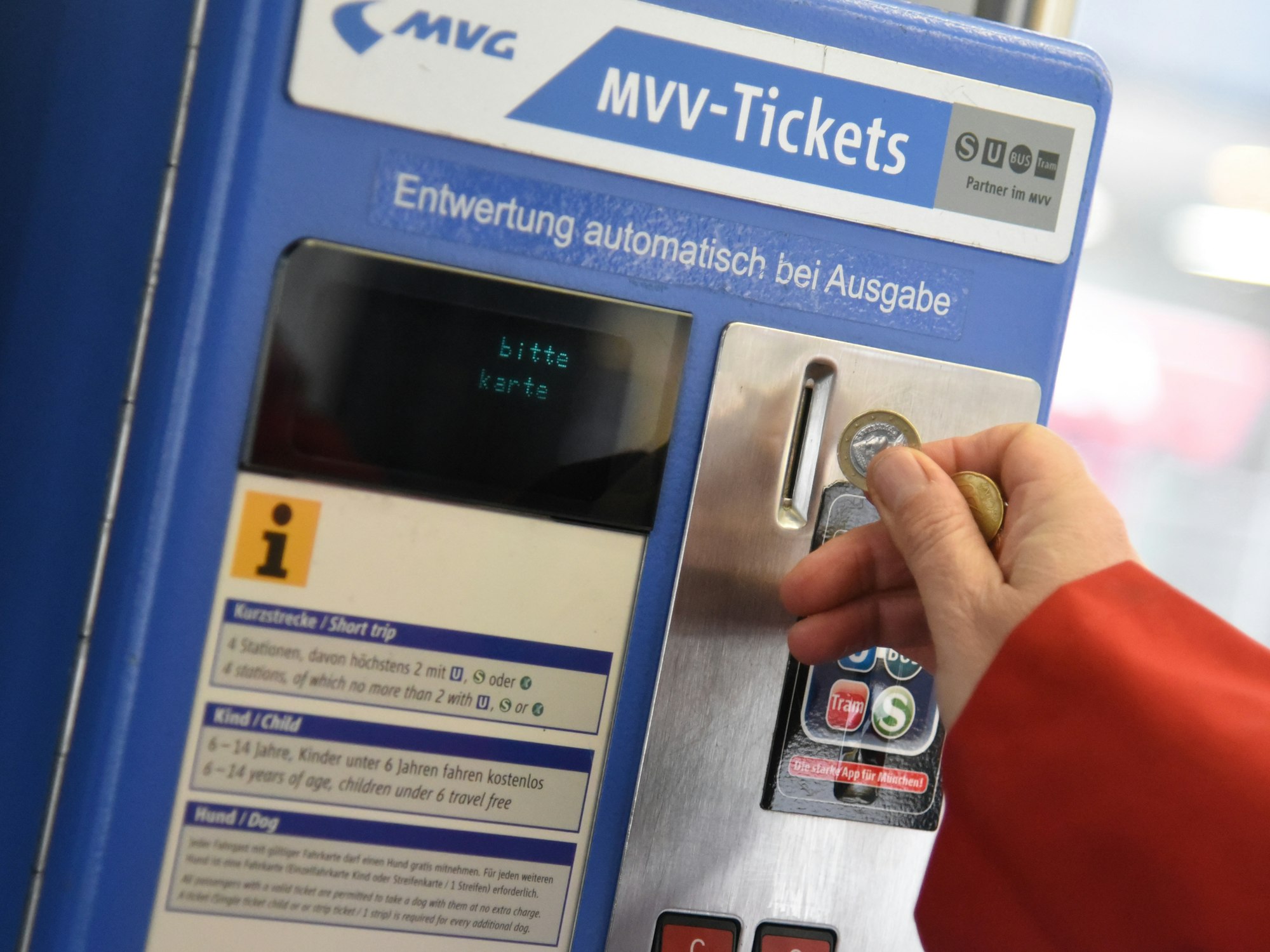 Eine Person wirft Münzen in einen Automaten des Münchner Verkehrs- und Tarifverbunds