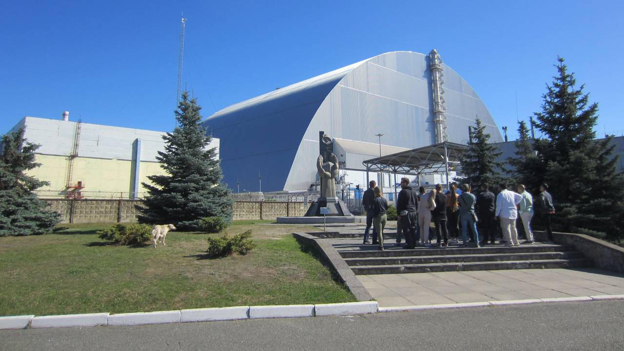 Touristengruppe am Mahnmal vor dem 1986 explodierten Blocks vier des Atomkraftwerks Tschernobyl in der Ukraine. Vor dem geschützten Block steht eine Statue, davor steht eine Gruppe von Touristen.