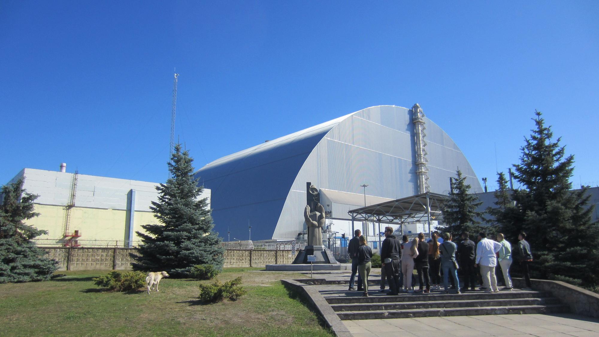 Touristengruppe am Mahnmal vor dem 1986 explodierten Blocks vier des Atomkraftwerks Tschernobyl in der Ukraine. Vor dem geschützten Block steht eine Statue, davor steht eine Gruppe von Touristen.