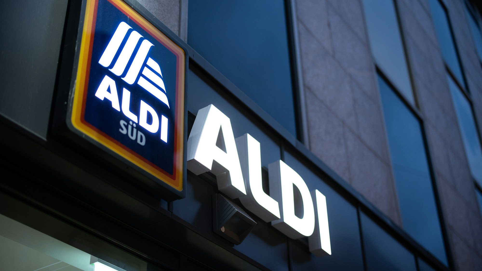 Das Logo einer Aldi Süd Filiale, fotografiert im November 2020 in einer Fußgängerzone der Düsseldorfer Innenstadt. Das Logo leuchtet, es ist Abend.