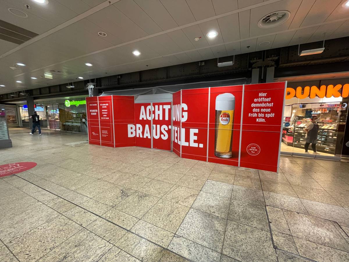 Ein Bauschild mit der Aufschrift „Achtung Braustelle“ steht im Kölner Hauptbahnhof und kündigt das neue Lokal der Brauerei Früh an.