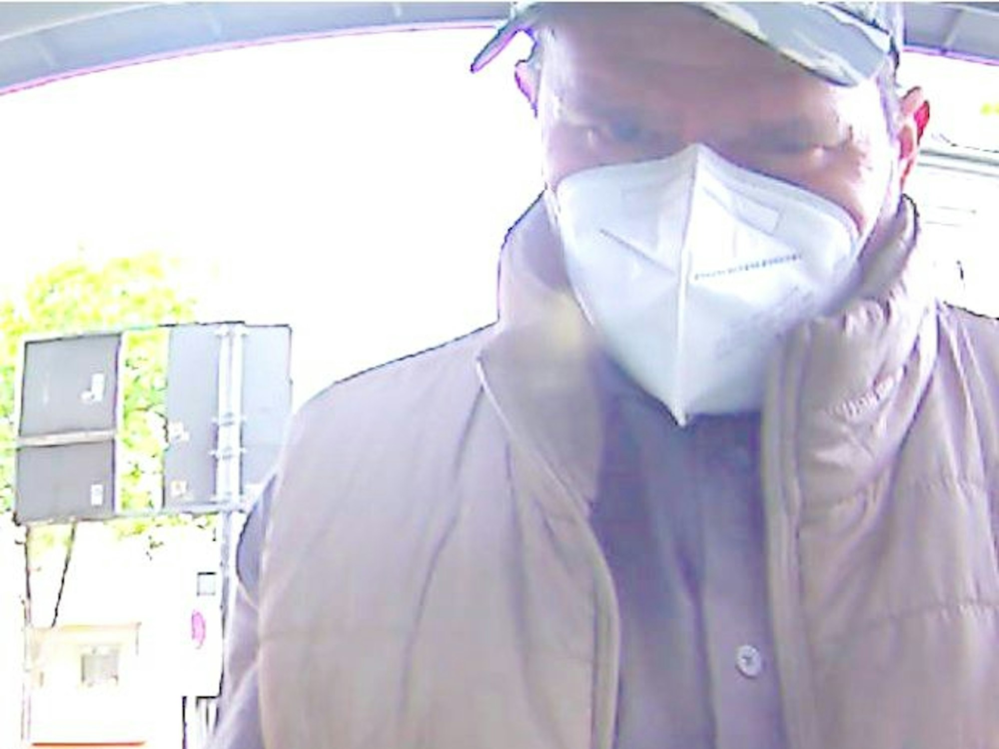 Mann mit Kappe und Corona-Schutzmaske beim Geldabheben am Automaten