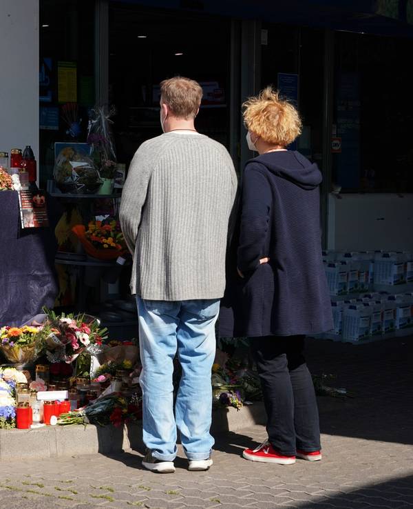 Blumen, Kerzen und Botschaften an das Opfer liegen am 21. September an der Tankstelle in der Innenstadt von Idar-Oberstein. Menschen stehen davor mit gefalteten Händen und gedenken des Opfers.
