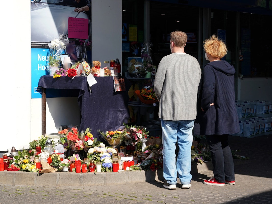 Blumen, Kerzen und Botschaften an das Opfer liegen am 21. September an der Tankstelle in der Innenstadt von Idar-Oberstein. Menschen stehen davor mit gefalteten Händen und gedenken des Opfers.