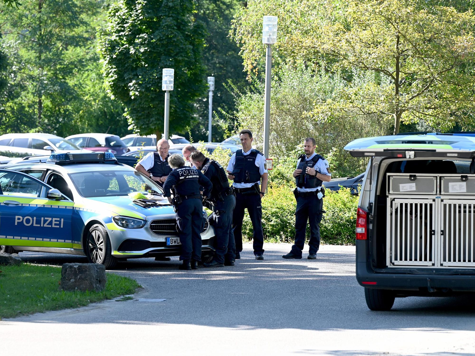 Polizisten besprechen sich vor der Klinik am Weissenhof, sie haben eine Karte auf der Motorhaube ausgebreitet. Auch ein Wagen mit einer Box für einen Spürhund ist zu sehen.