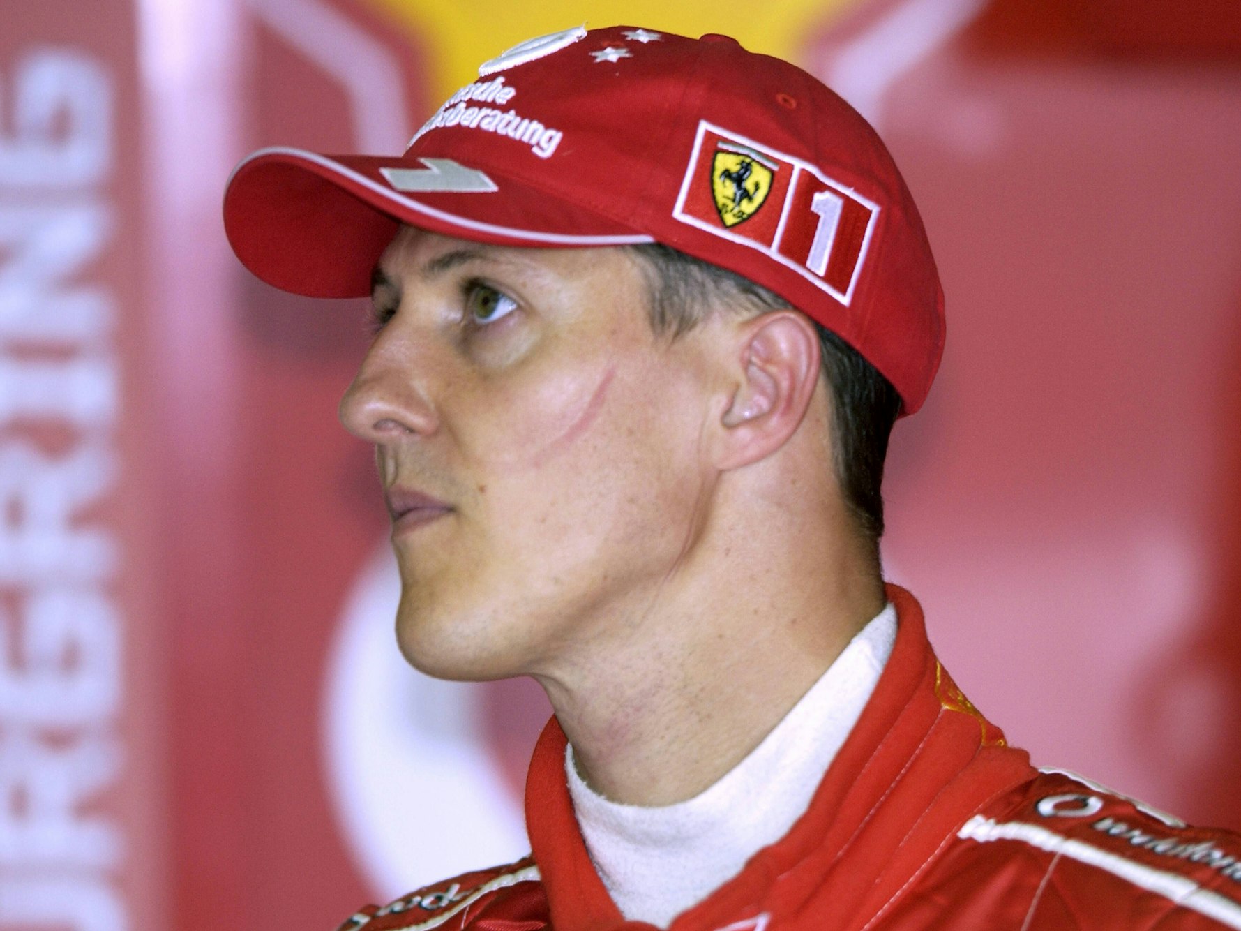 Michael Schumacher trägt einen roten Ferrari-Anzug eine rote Ferrari-Kappe.