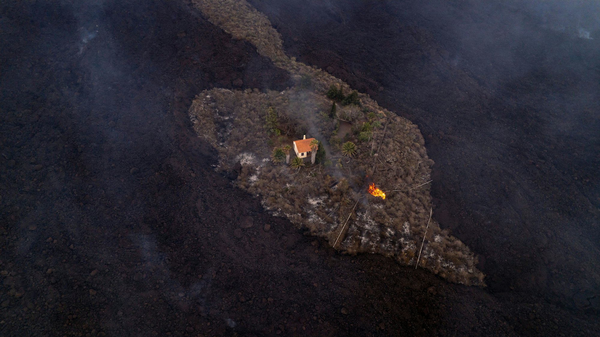 Auf diesem von iLoveTheWorld zur Verfügung gestellten Foto bleibt ein Haus intakt, während Lava fließt, nachdem ein Vulkan in der Nähe von Las Manchas auf der Insel La Palma ausgebrochen ist. Der Vulkan war am 19. September erstmals seit 50 Jahren wieder aktiv geworden.