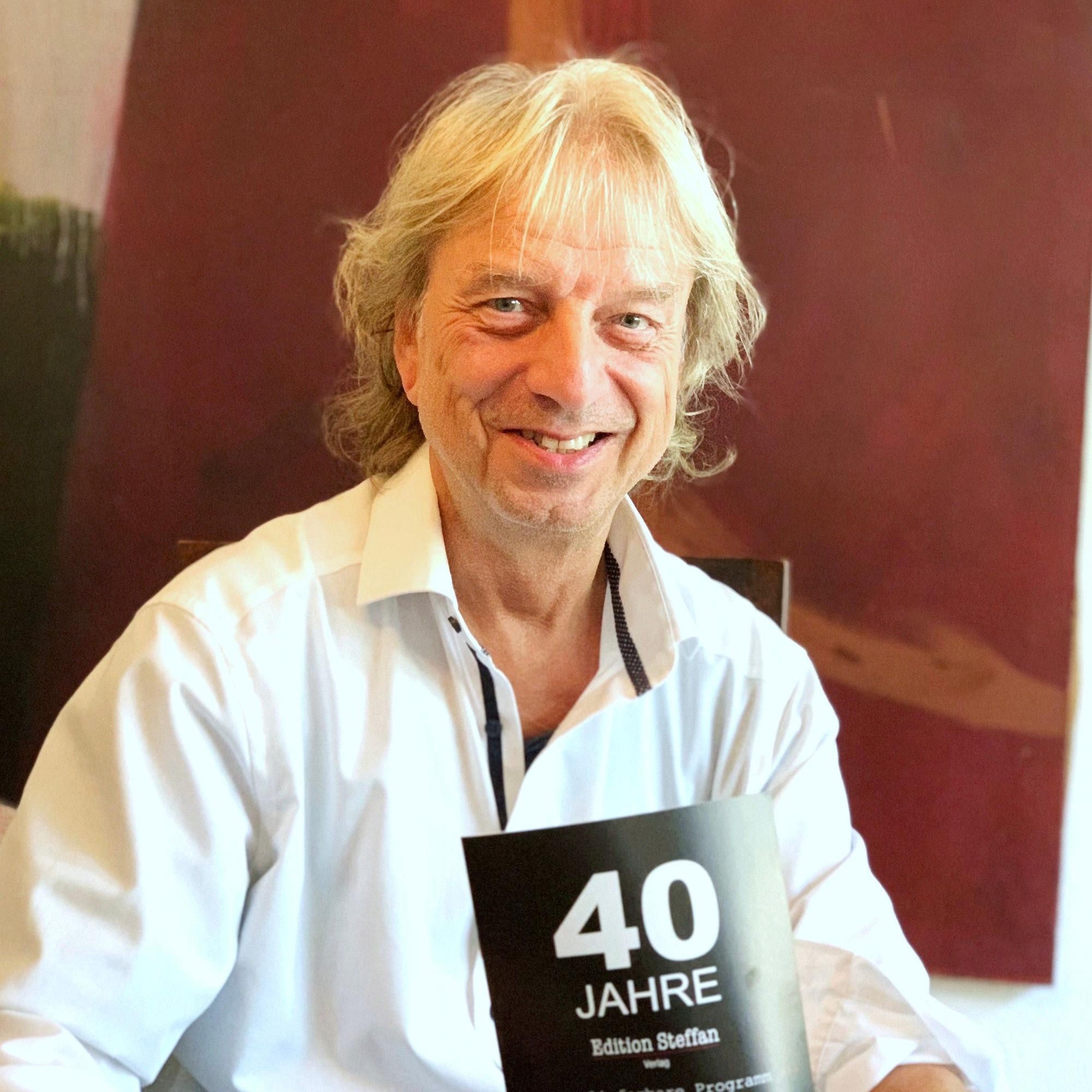 Frank Steffan hält ein Prospekt zu seinem Firmenjubiläum in den Händen.